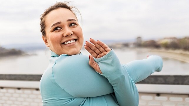 A woman smiling while outside stretching before exercising.
