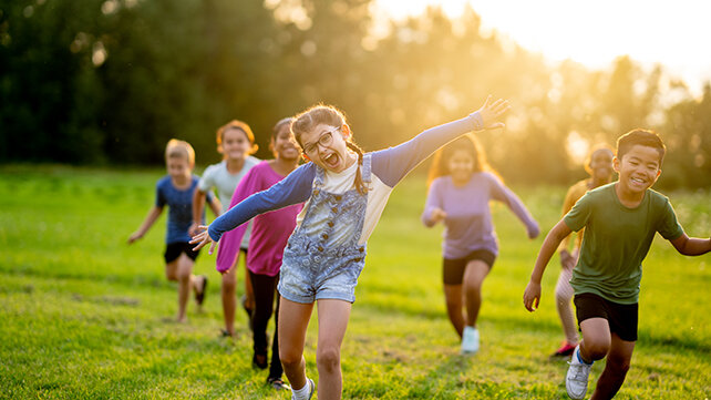 6 school-age children running in field toward camera late afternoon