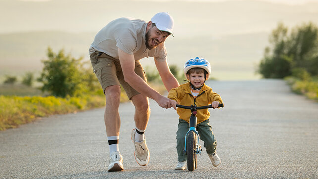 A man helps a young child ride a bicycle.