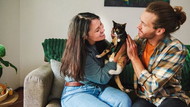 A smiling couple sitting on their couch and holding their cat