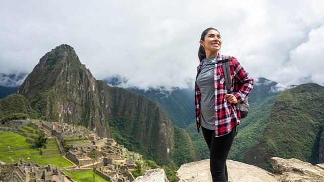 Woman, wearing a backpack and hiking clothes, standing outdoors while traveling abroad
