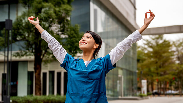A smiling doctor looking upward with her arms open