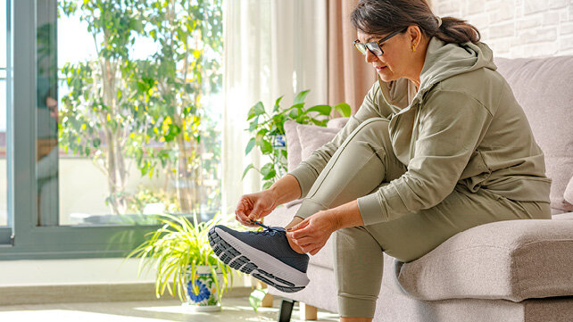 Woman in a track suit, sitting on her couch, and tying one of her sneakers.