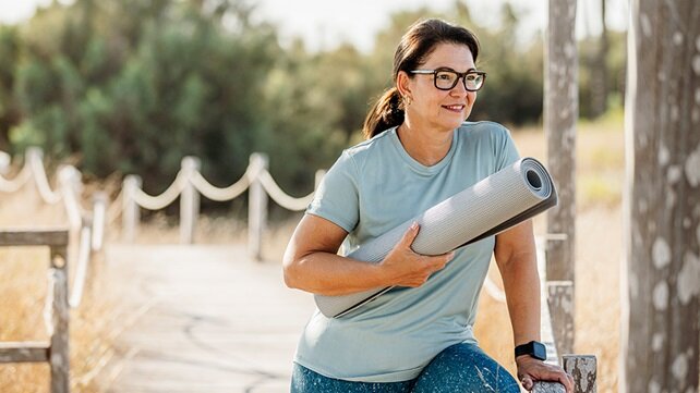 Adult woman carrying a yoga mat as she walks outside on a nice day.