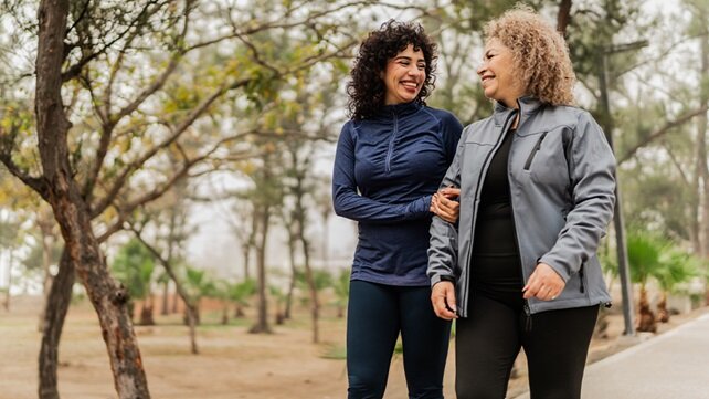 An adult daughter and her mother walking outside in a park in the fall.
