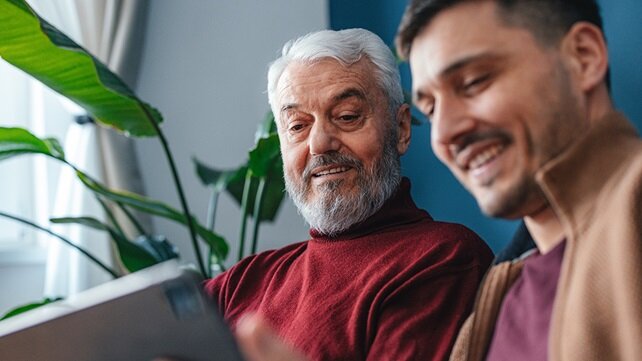 An adult male looking at something on tablet with his father.