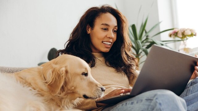 Woman sitting on her couch with her laptop and golden retreiver.