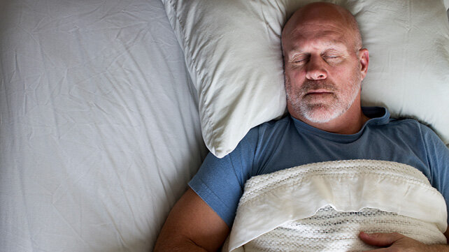 Adult male asleep on his beck in his bed.