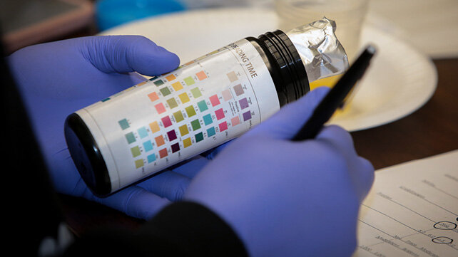 A pair of hands wearing medical-grade PPE glvoes holding a labeled bottle.