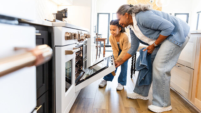 A grandmother and her granddaughter bending down to see the food cooking in the oven.