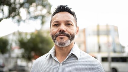 Man in striped shirt looking at camera outdoors with building in background