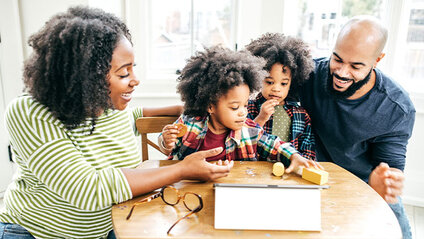 Two adults and two children playing a game while sitting at a table.