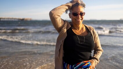 A person standing on a beach with waves and a pier in the background.